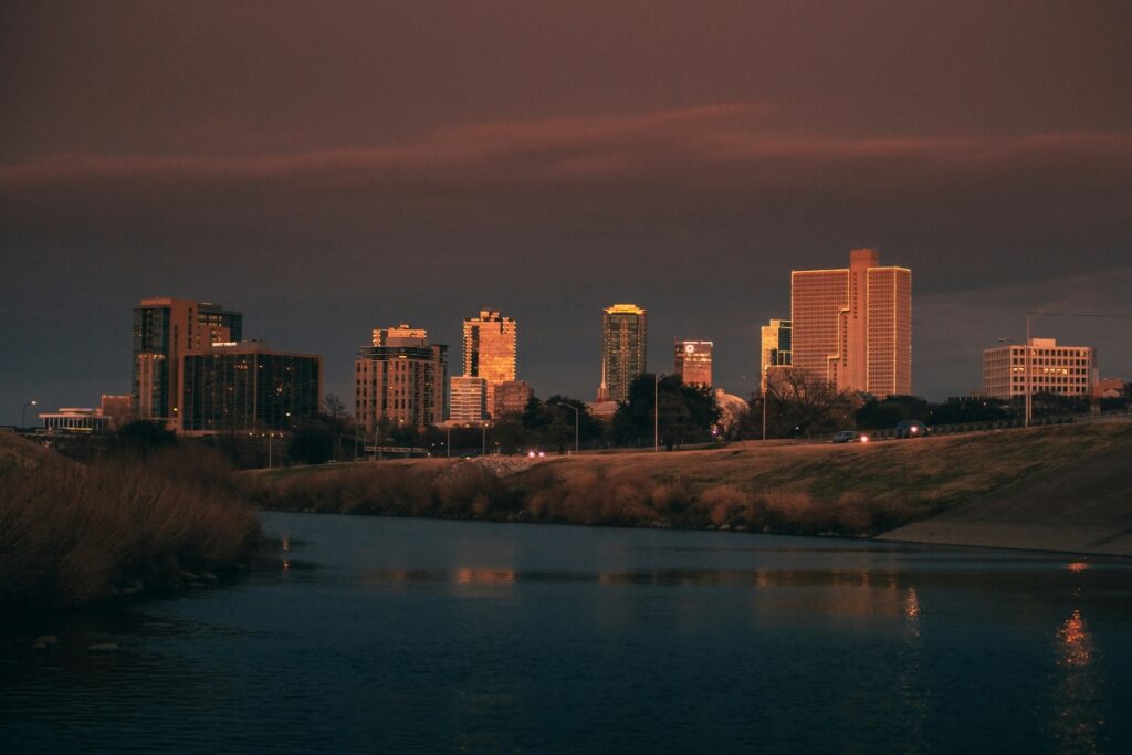Fort Worth, Texas skyline at sunset with buildings reflecting warm light over the Trinity River