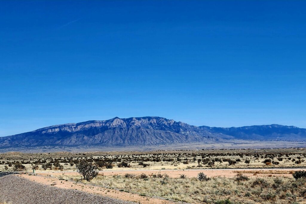 View of Rio Rancho, New Mexico desert landscape with sparse vegetation and Sandia Mountains in the background under a clear blue sky